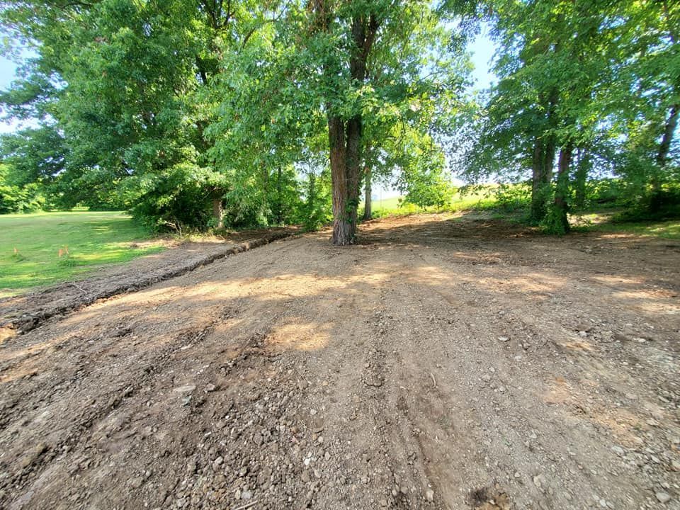 A dirt road going through a field with trees in the background.