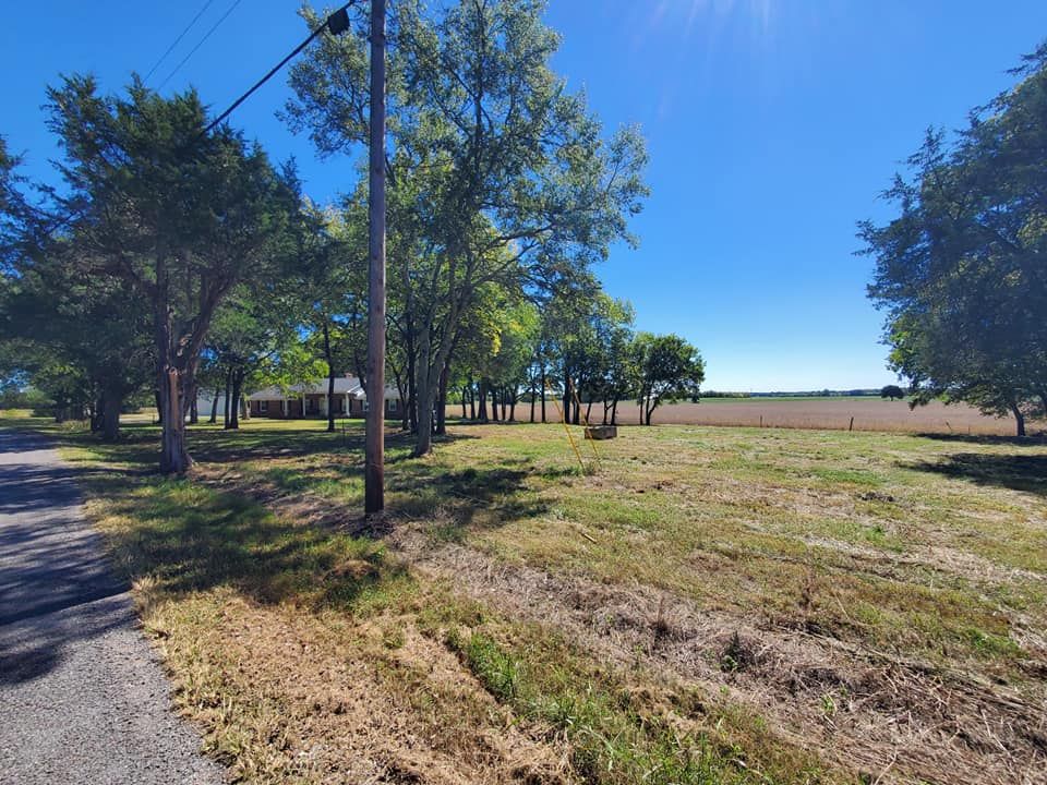 A large grassy field with trees and a house in the background.