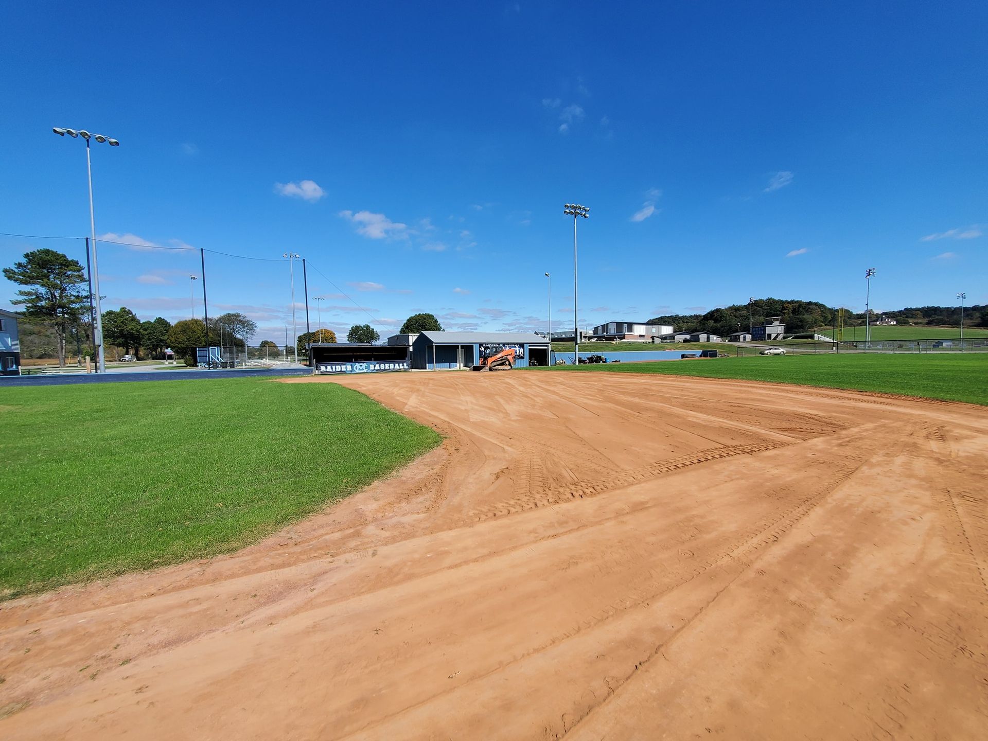 A dirt road leading to a baseball field on a sunny day.