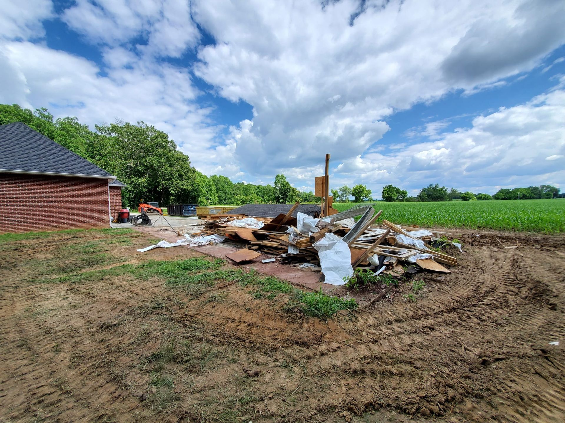 A pile of trash is sitting in the middle of a dirt field in front of a house.
