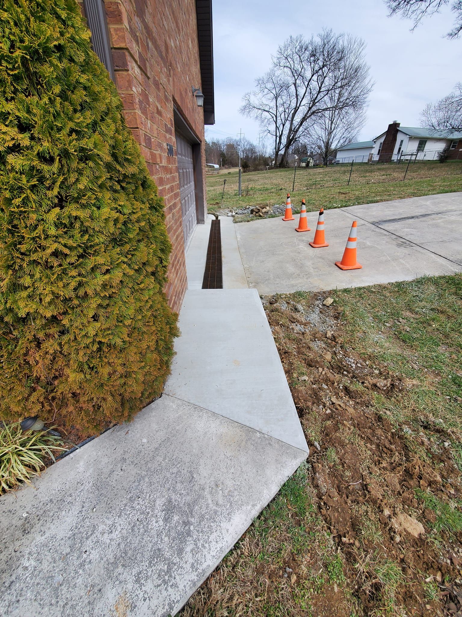 A concrete sidewalk next to a brick building with orange traffic cones.