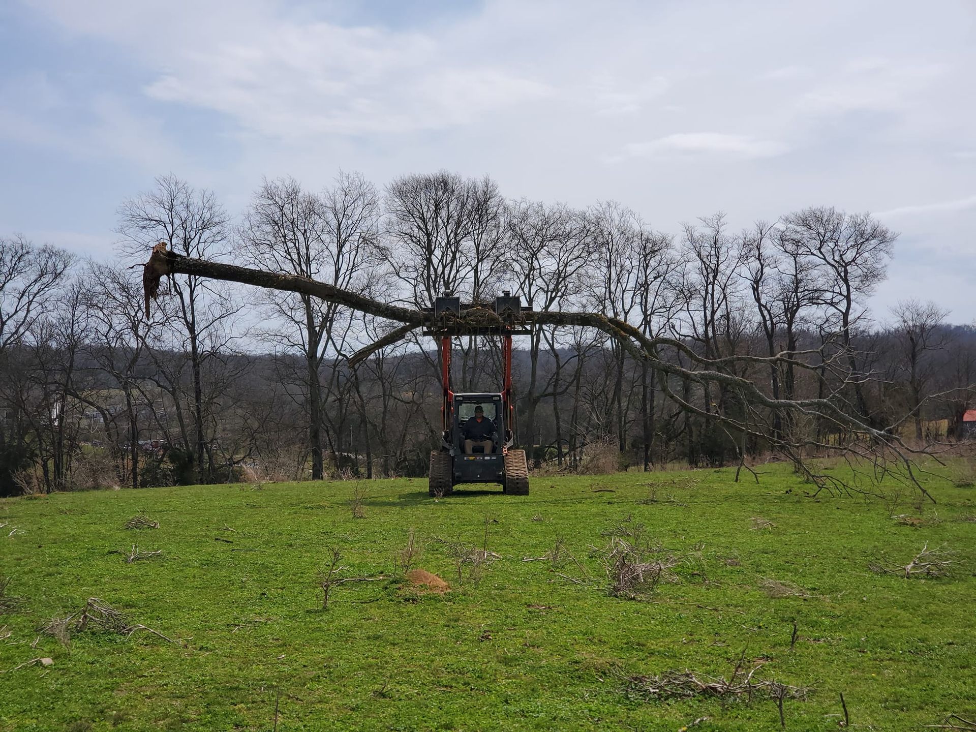 A tractor is driving through a grassy field with trees in the background.