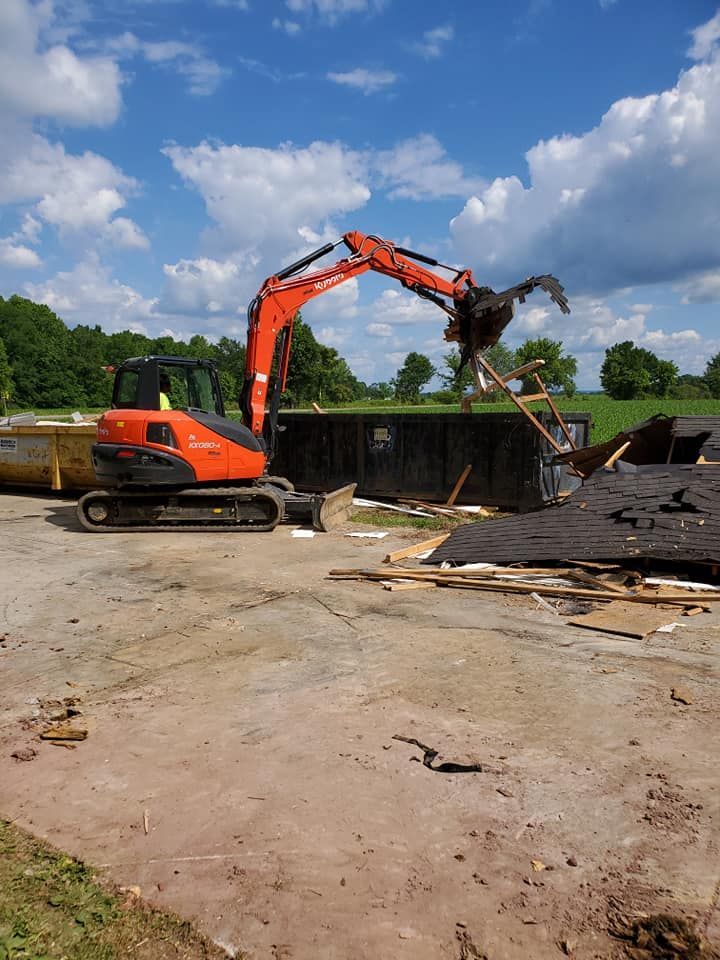 A large orange excavator is demolishing a building in a dirt field.
