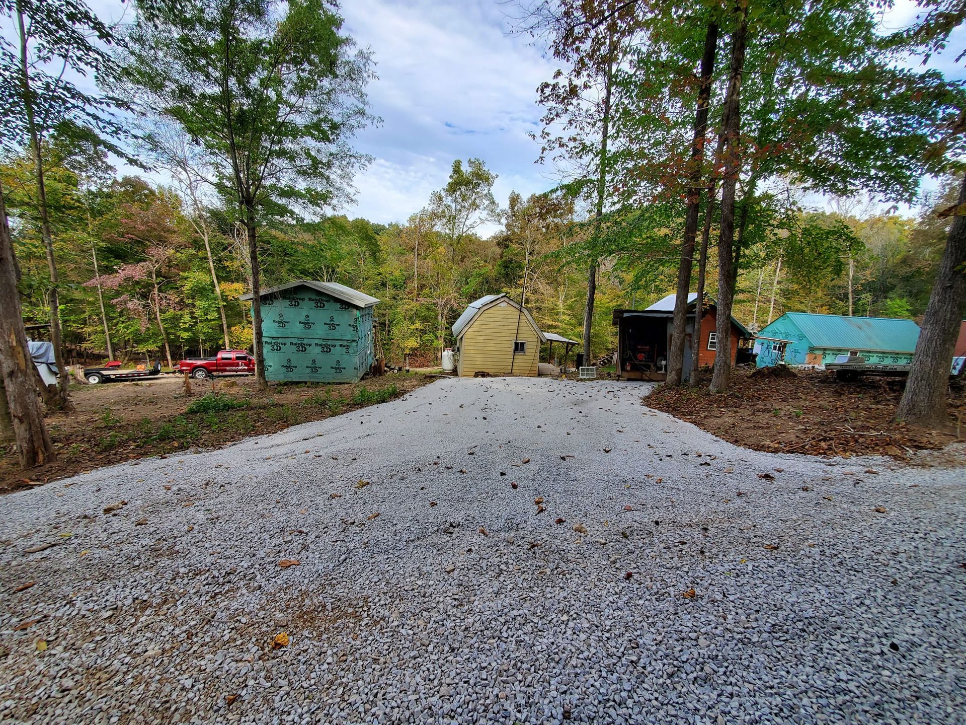 A gravel driveway leading to a house in the woods.