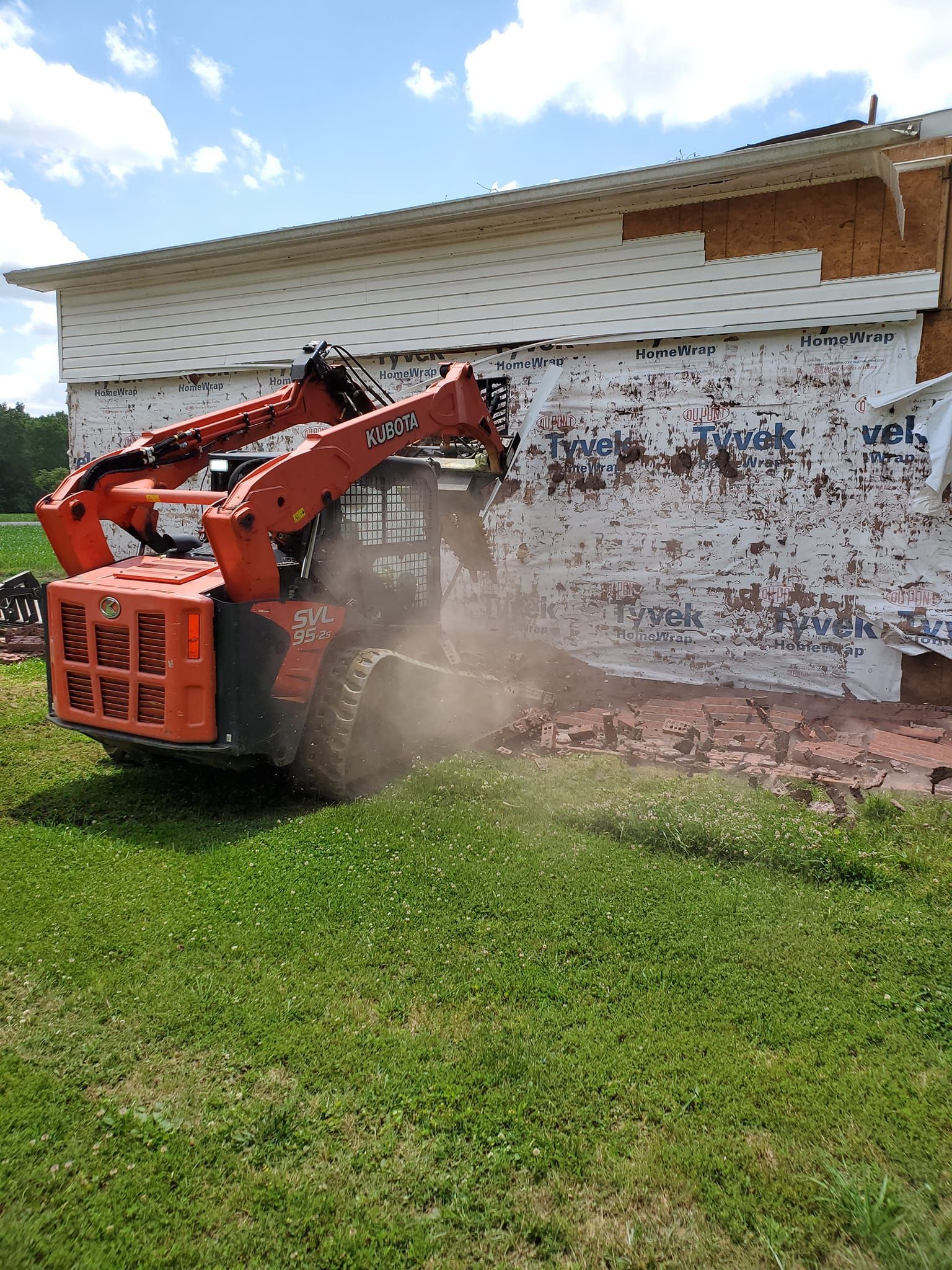A bulldozer is demolishing a white building in a grassy field.