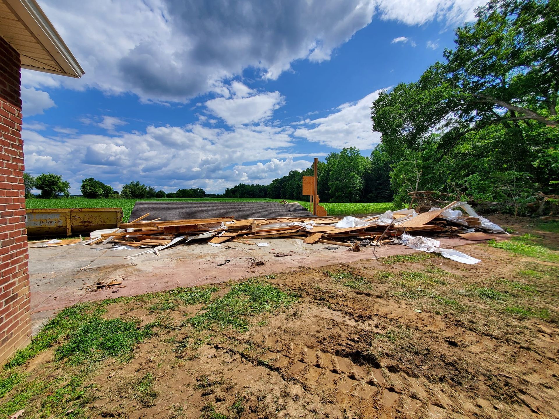 A pile of wood is sitting in the middle of a dirt field next to a brick building.