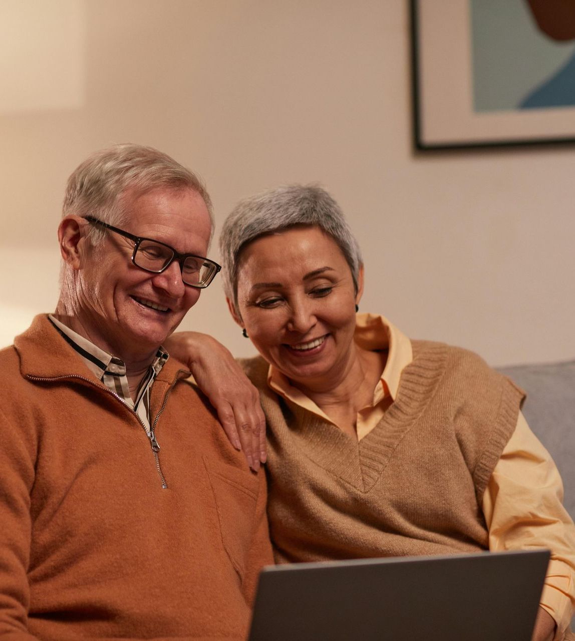A man and a woman are sitting on a couch looking at a laptop computer.