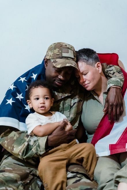 A man in a military uniform is sitting on a couch with a woman and a child.