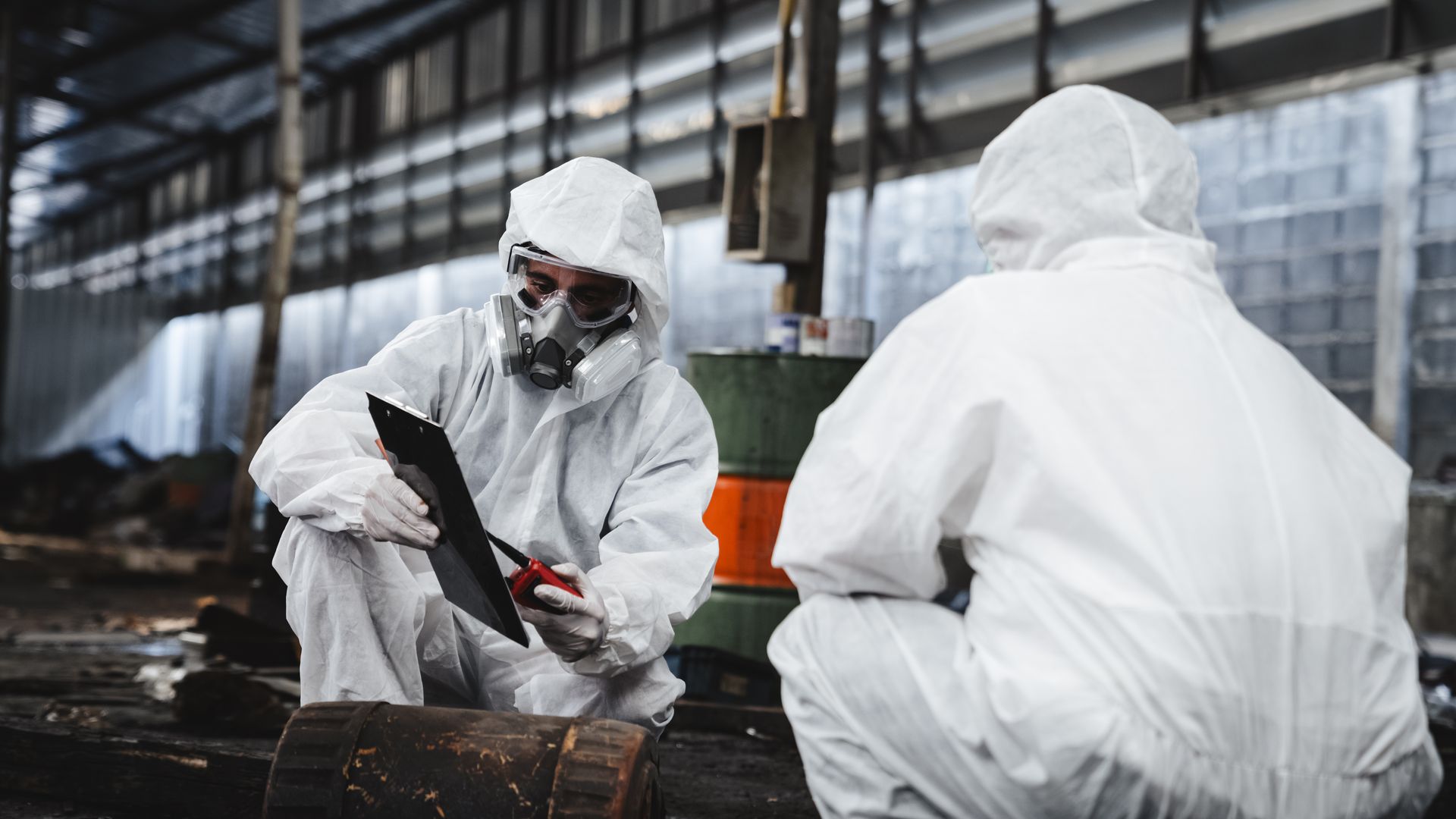 Workers wearing full-body protective clothing while working with the asbestos roof tiles. Workers wearing full-body protective clothing while working with the asbestos roof tiles.