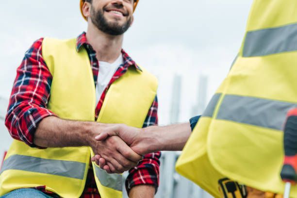 Two construction workers are shaking hands on a construction site.