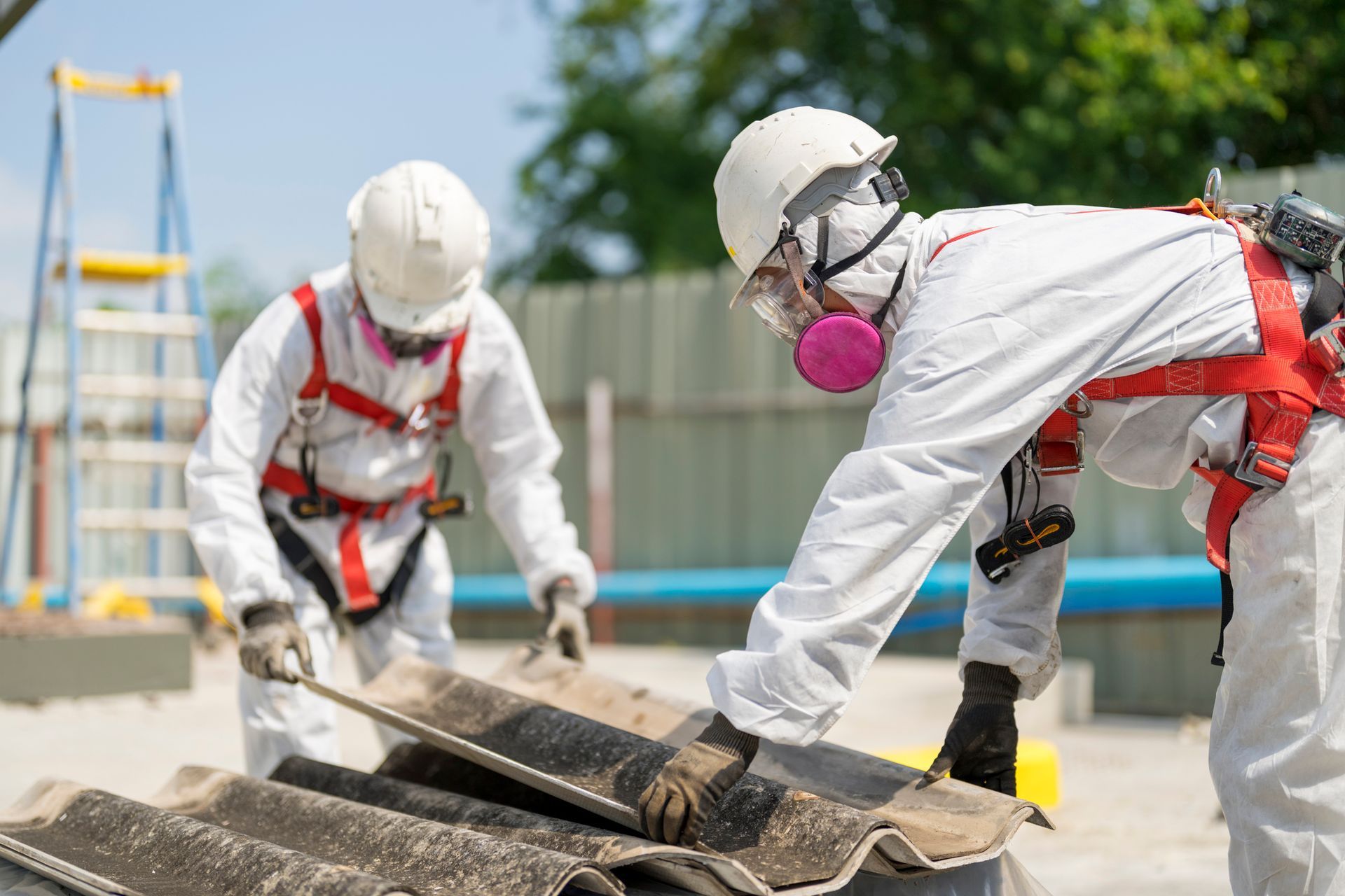 Construction workers handling asbestos roofing sheets at construction site, protective gear.