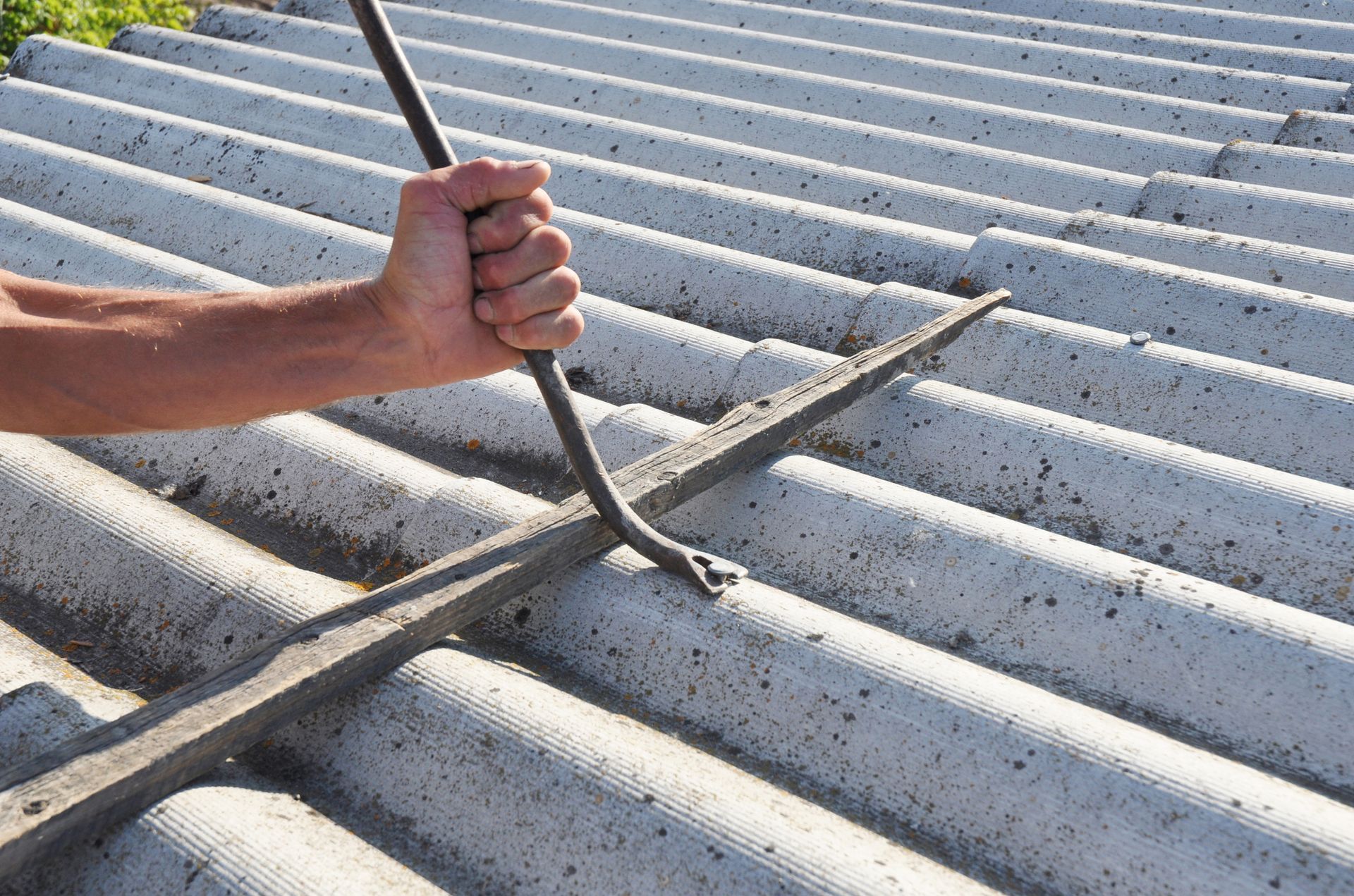 Close-up of an asbestos removal by a roofer by safely using a crowbar for handling.