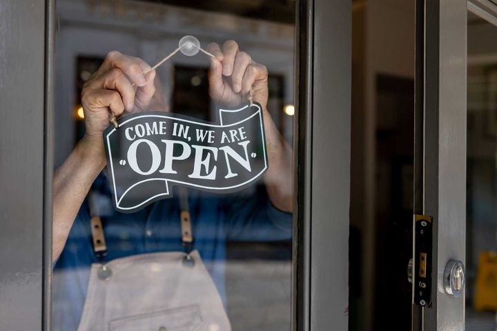 A man is hanging an open sign on a glass door.