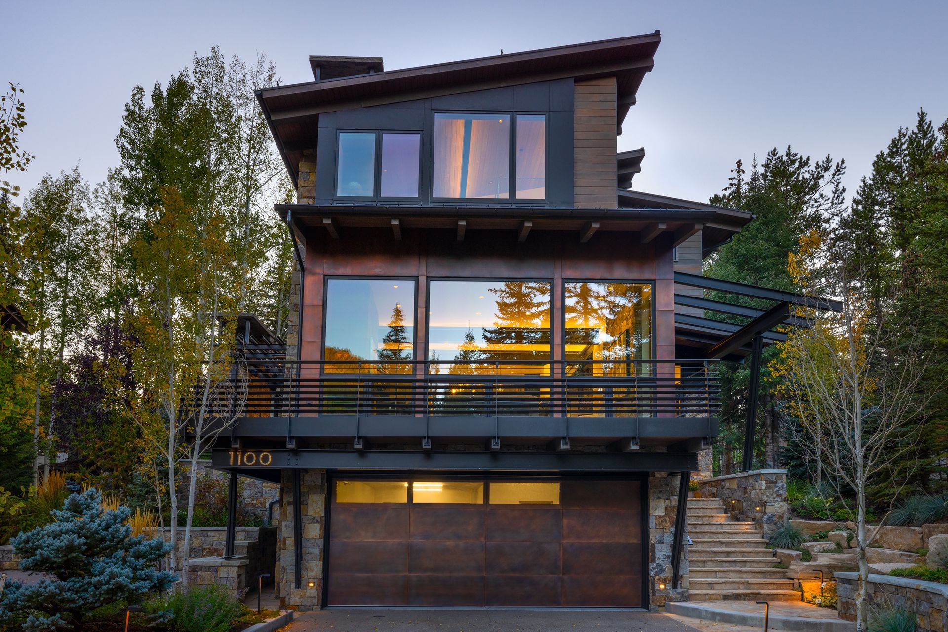 A modern house with a large garage and a balcony surrounded by trees.