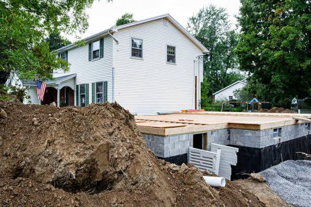 Home addition in base level of white home, with forest background and pile of dirt in front.