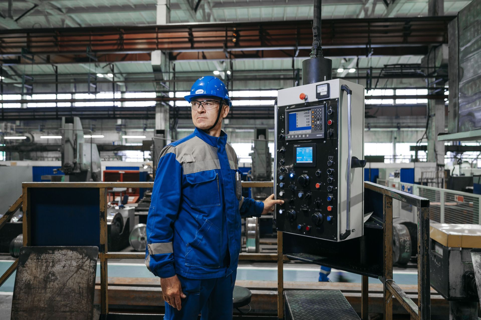 A manufacturing worker in a hard hat inspecting equipment on a factory production floor.