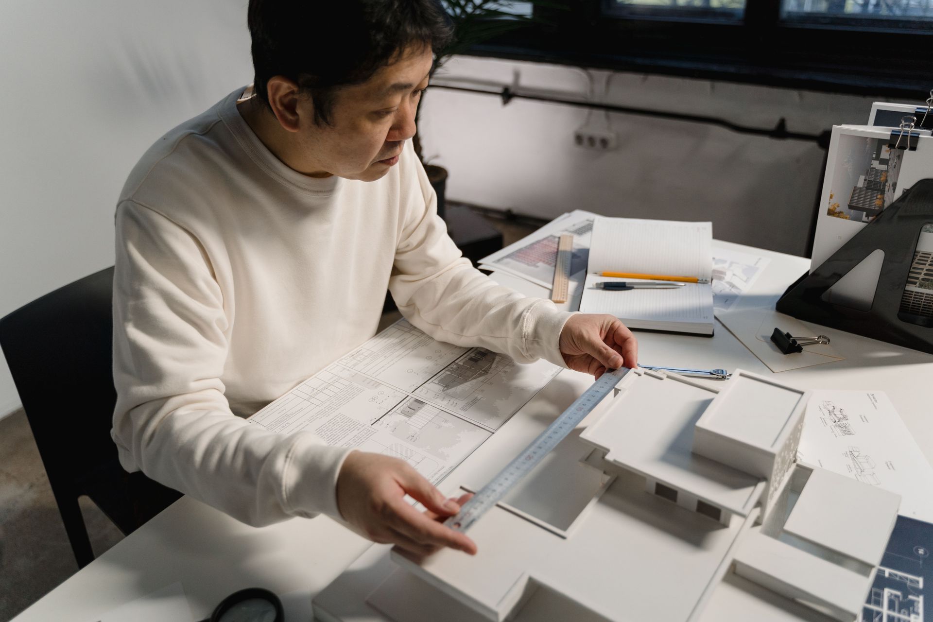 An architect reviewing building blueprints and a scale model at a desk in a modern studio.