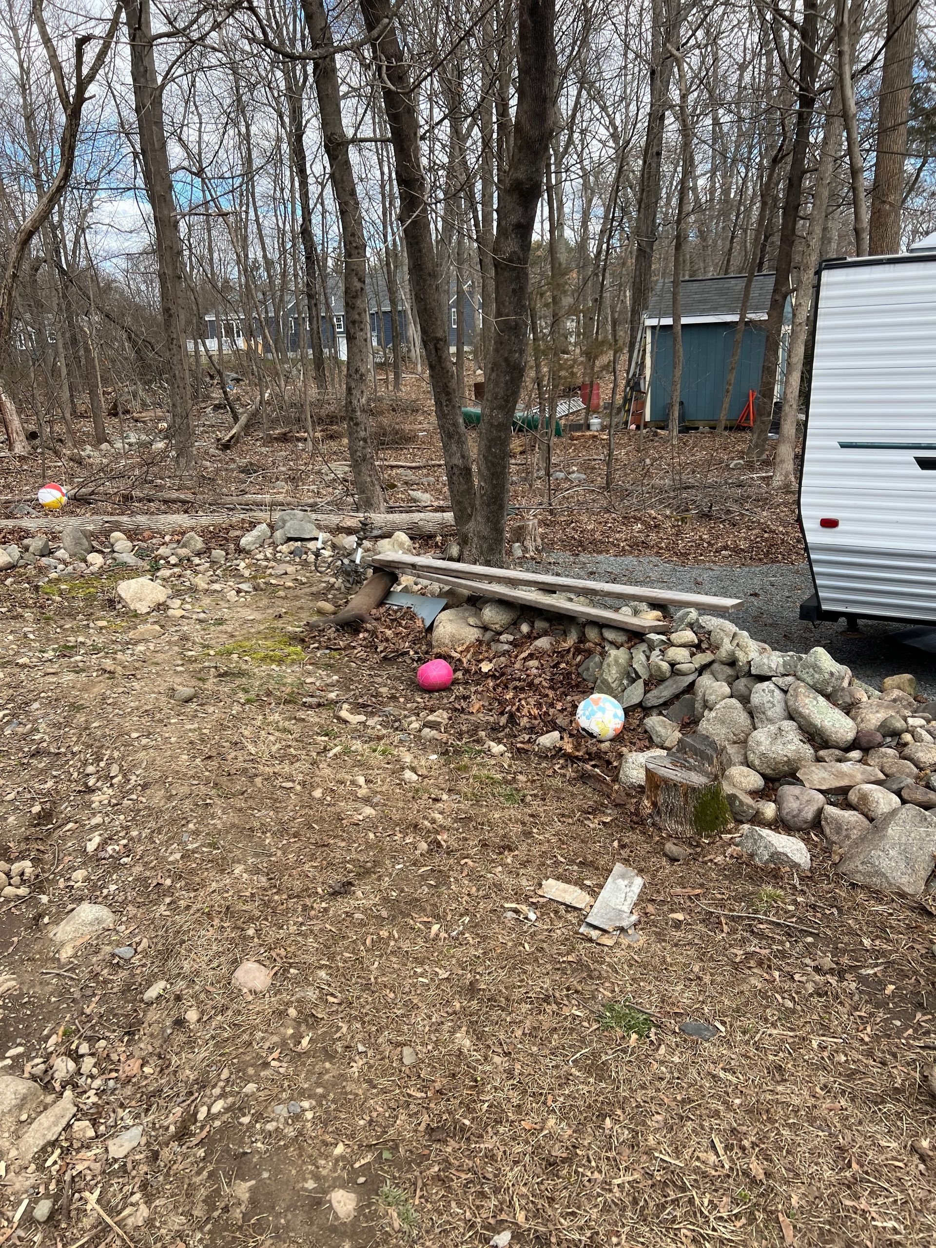 A trailer is parked in the woods next to a rock wall.