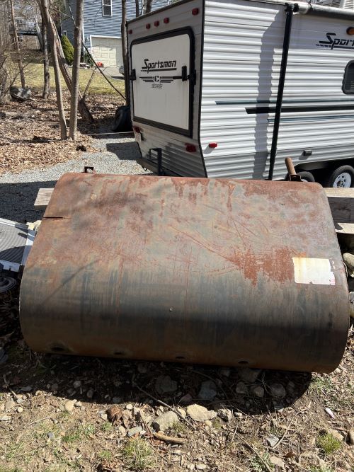 A rusty metal tank is sitting in the dirt in front of a trailer.