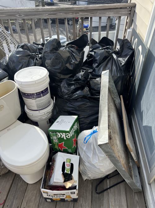 A pile of trash on a balcony next to a toilet and a box of heineken beer.