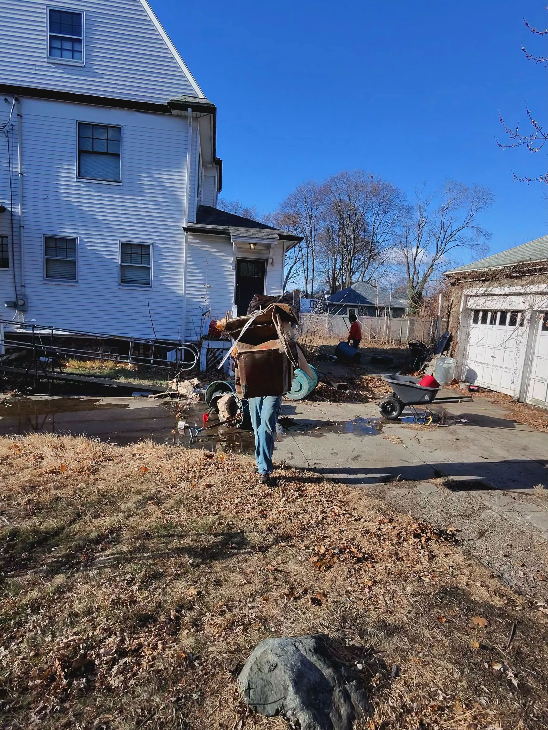 A man is carrying a large log on his back in front of a house.