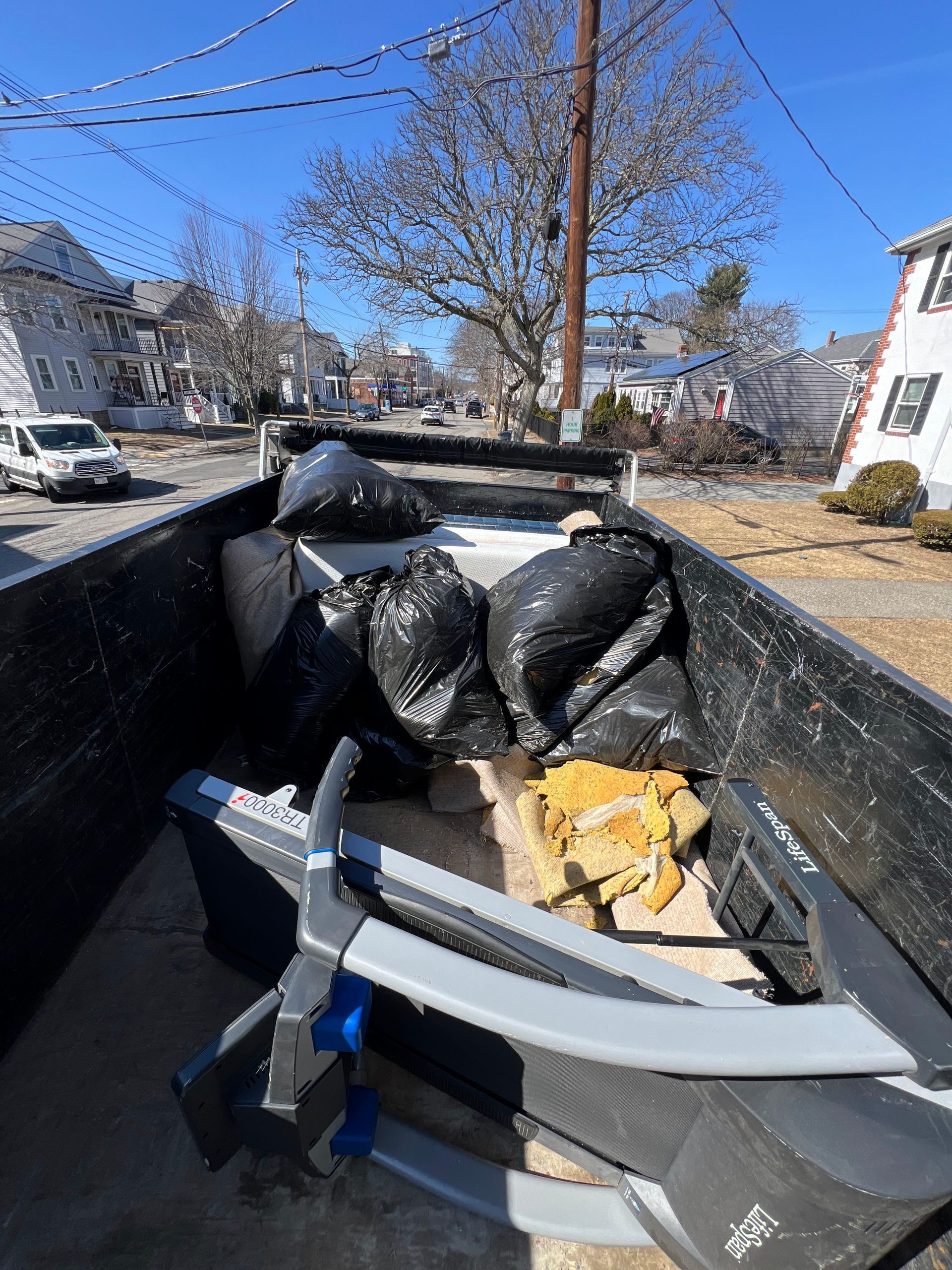 A dumpster filled with trash bags and a treadmill.