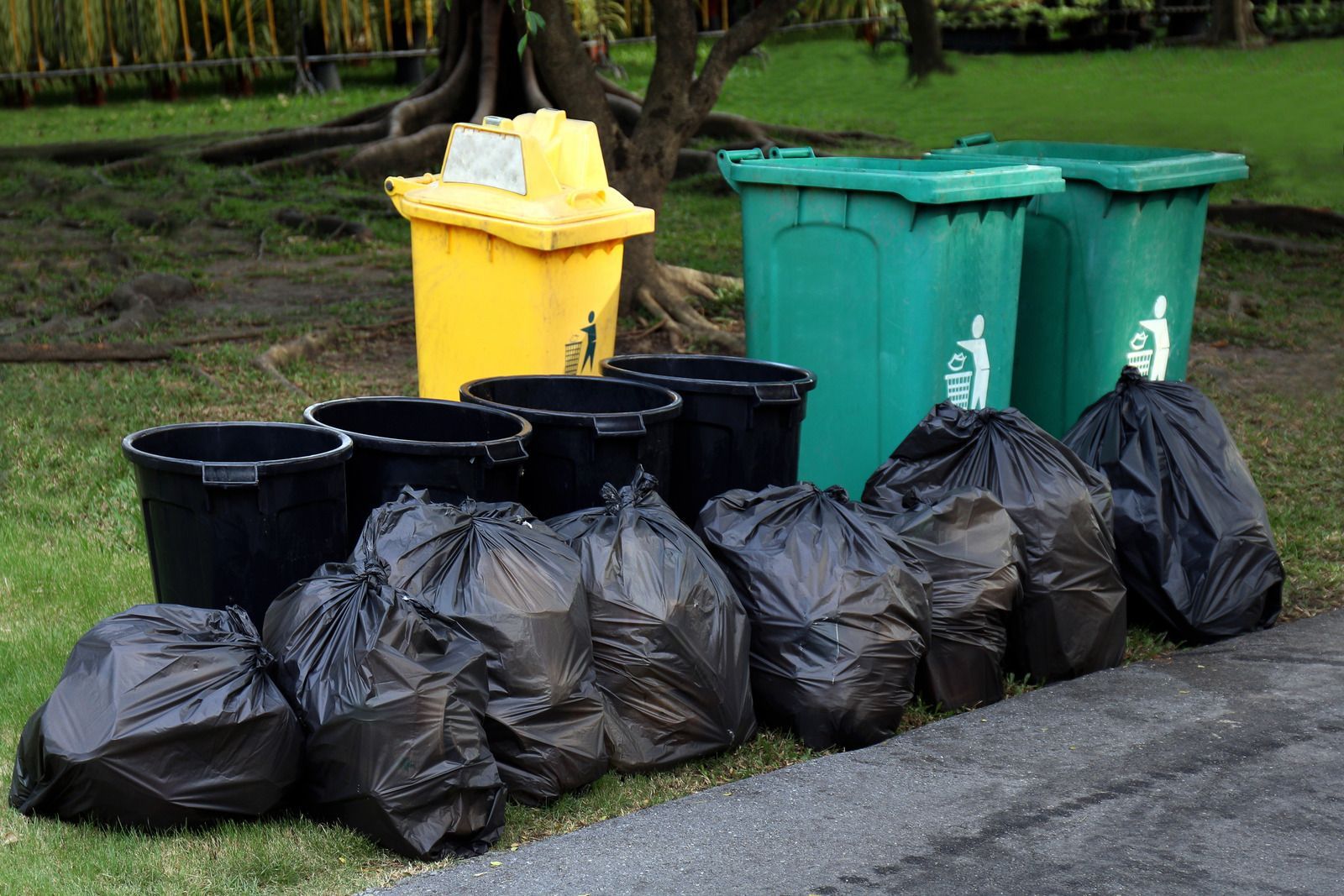 A bunch of garbage bags and trash cans on the side of the road