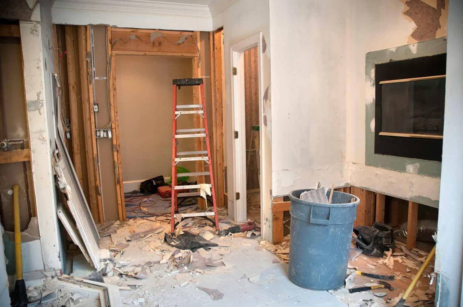 A room under construction with a ladder and a trash can.