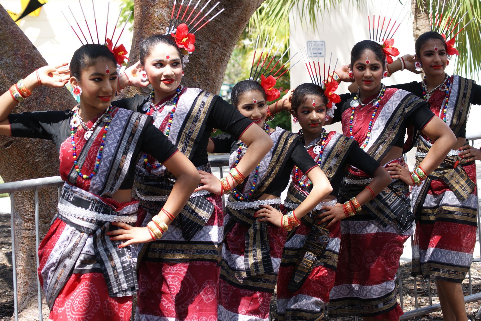 Group of women in traditional red and black attire, performing dance outdoors.