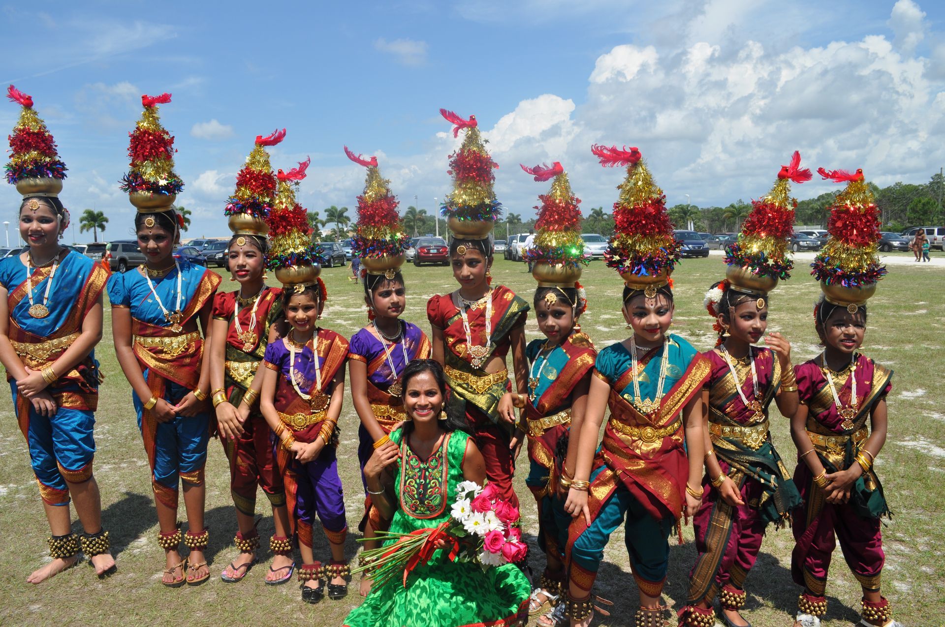 Group of girls in colorful traditional Indian dance costumes with pots on their heads, outdoors.