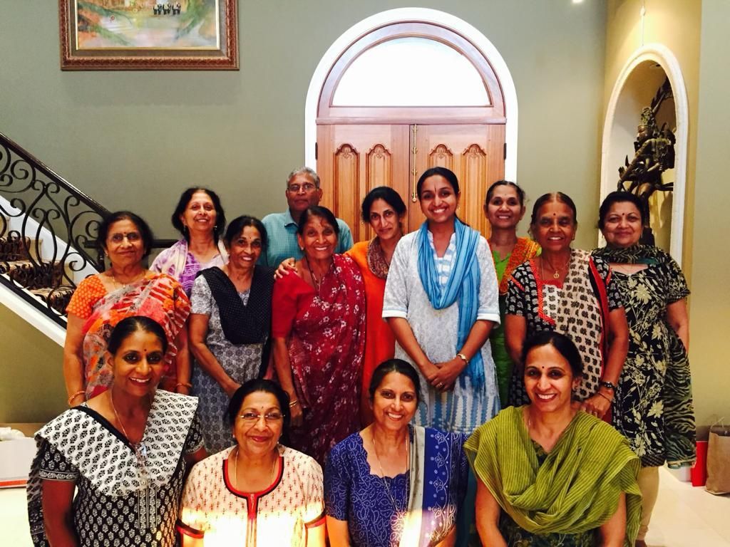 Group of women in saris pose inside a building with an arched doorway and a staircase.
