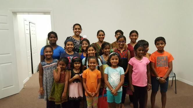 Group of smiling children and two women posing in a room, presumably a classroom.
