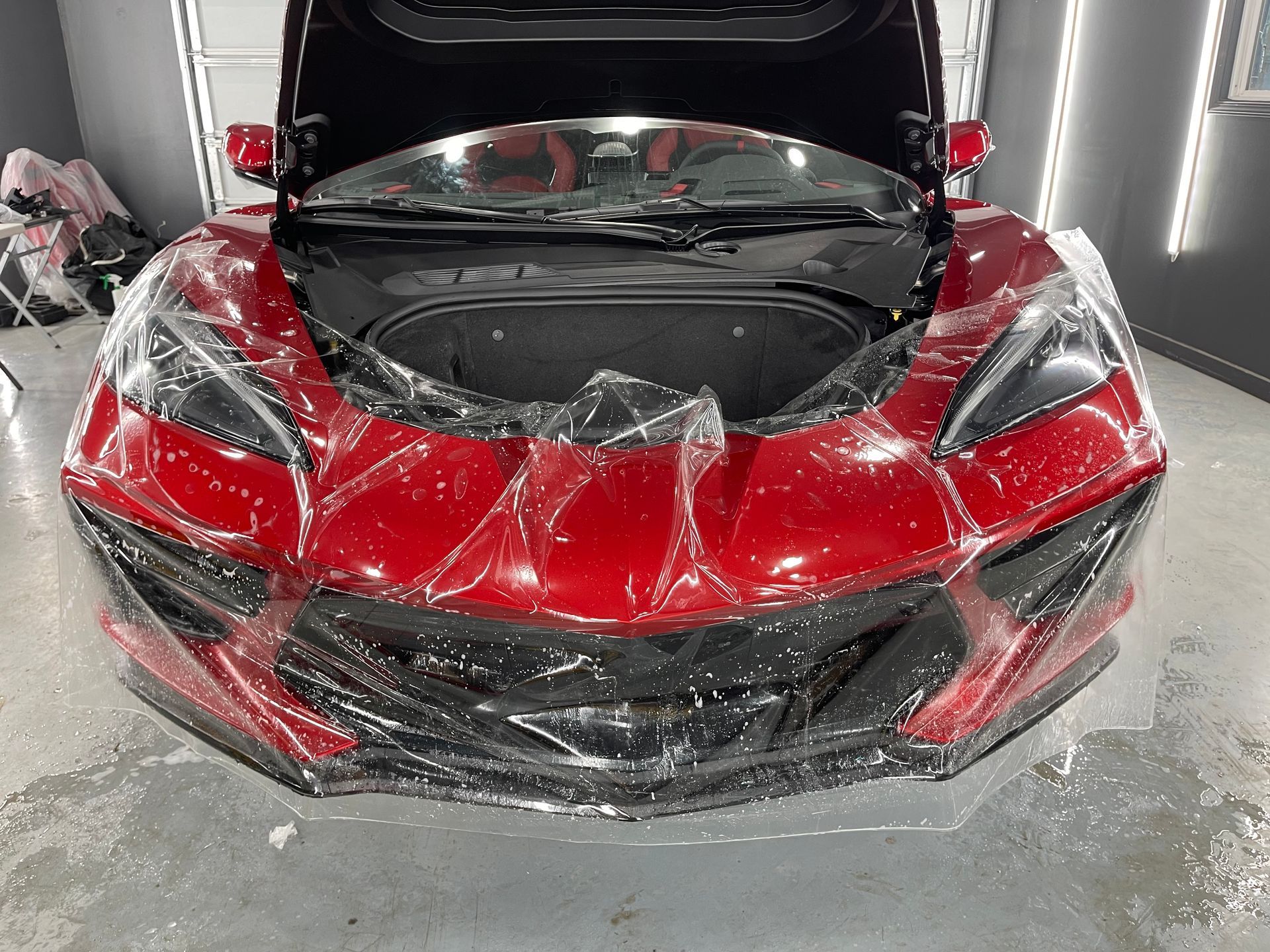 A red sports car with the hood up is wrapped in plastic.