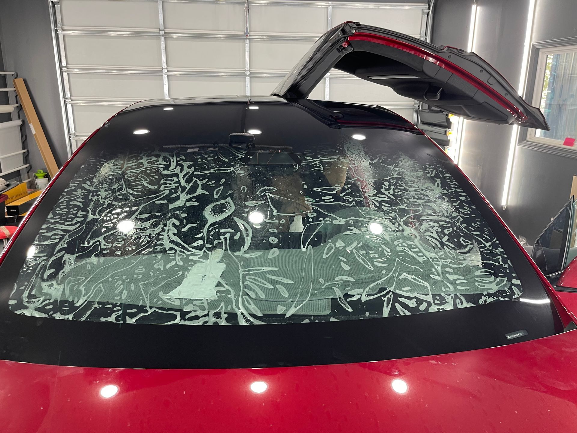 A red car with a black roof is sitting in a garage with its trunk open.