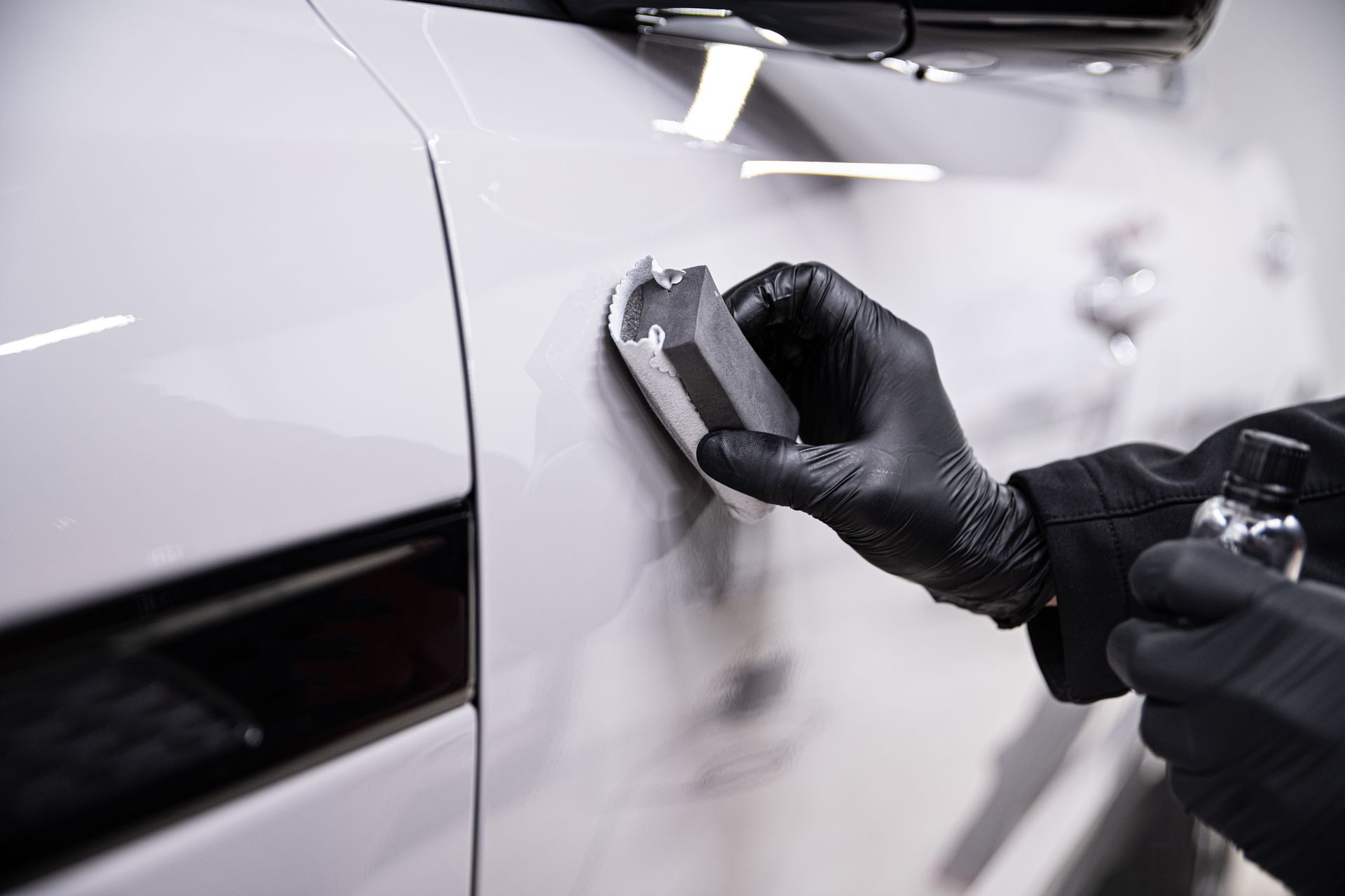 A person wearing black gloves is applying ceramic coating to a white car.