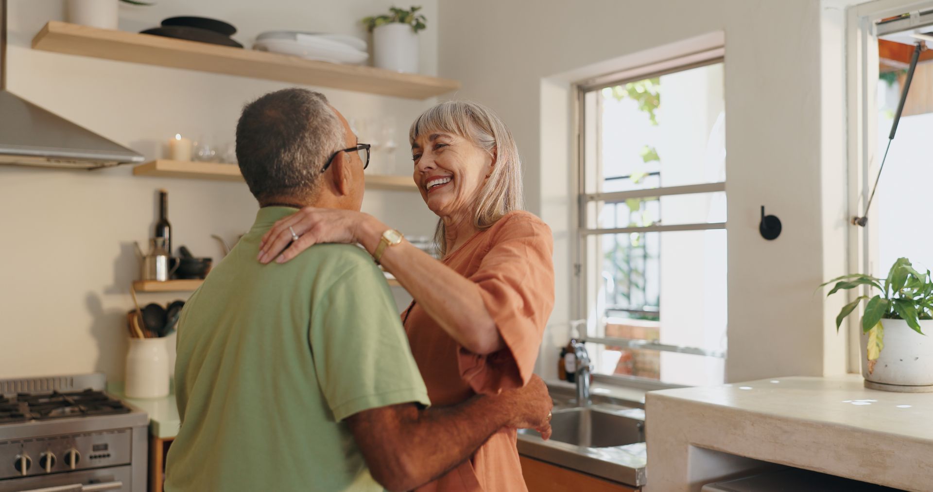 Couple dancing in a kitchen, smiling and embracing. Bright, natural light illuminates the space.