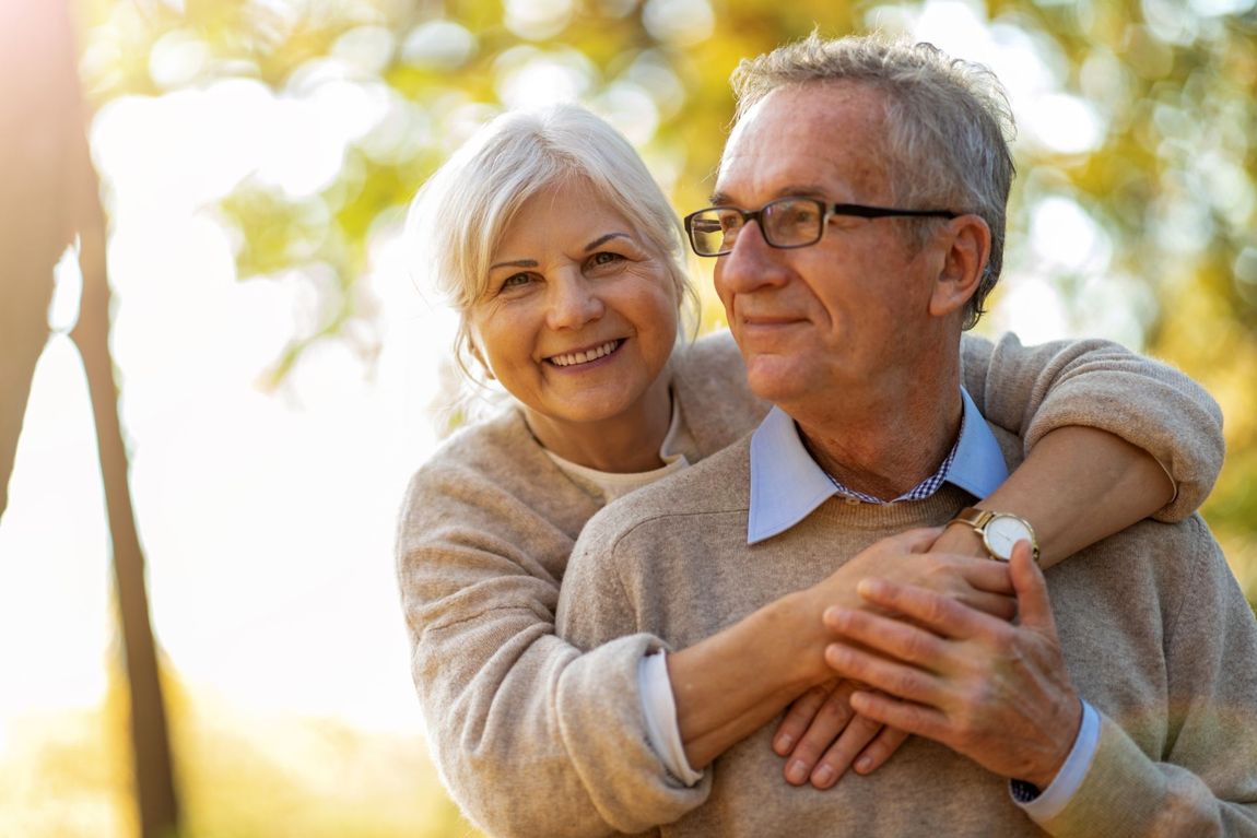 Smiling couple embracing outdoors. Woman hugs man, autumnal background, warm colors.