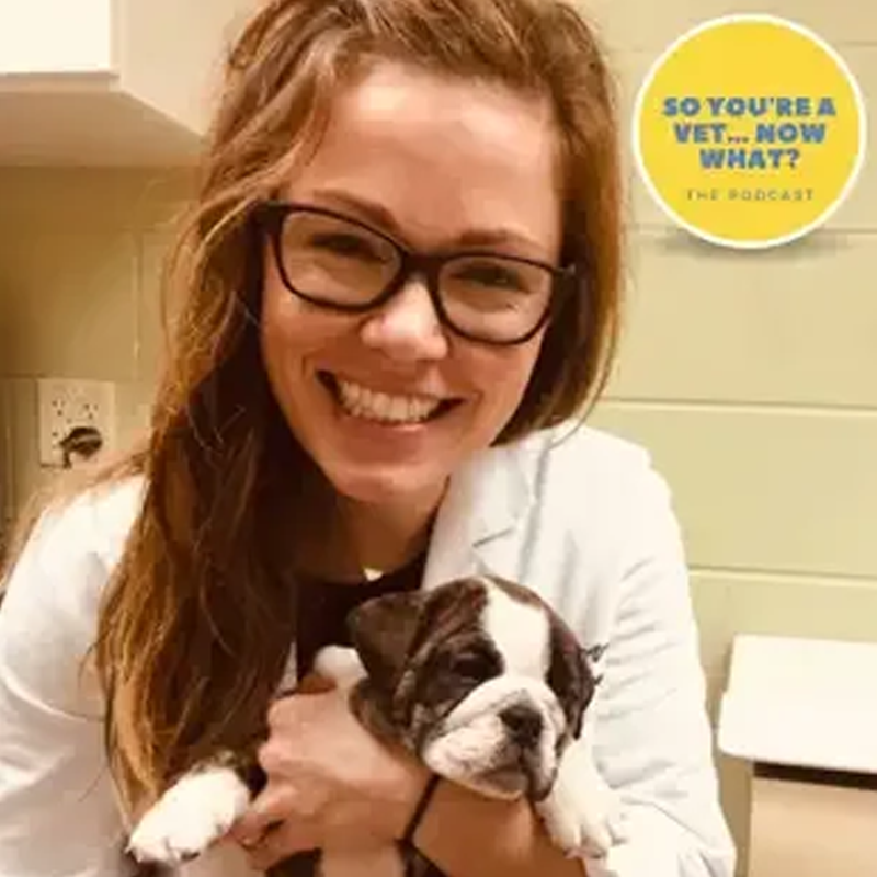 A woman in a lab coat is holding a puppy and smiling.