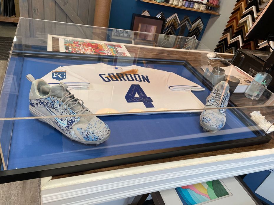 A Kansas City Royals Gordon number 4 jersey and matching patterned cleats displayed in a large, glass-topped shadow box.