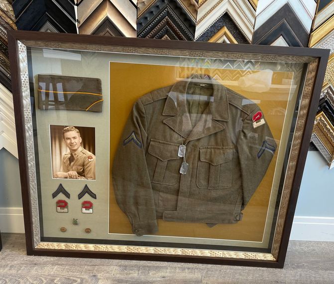 A military memorabilia shadow box containing a uniform jacket, dog tags, a photo, chevrons, and pins in a wooden frame.