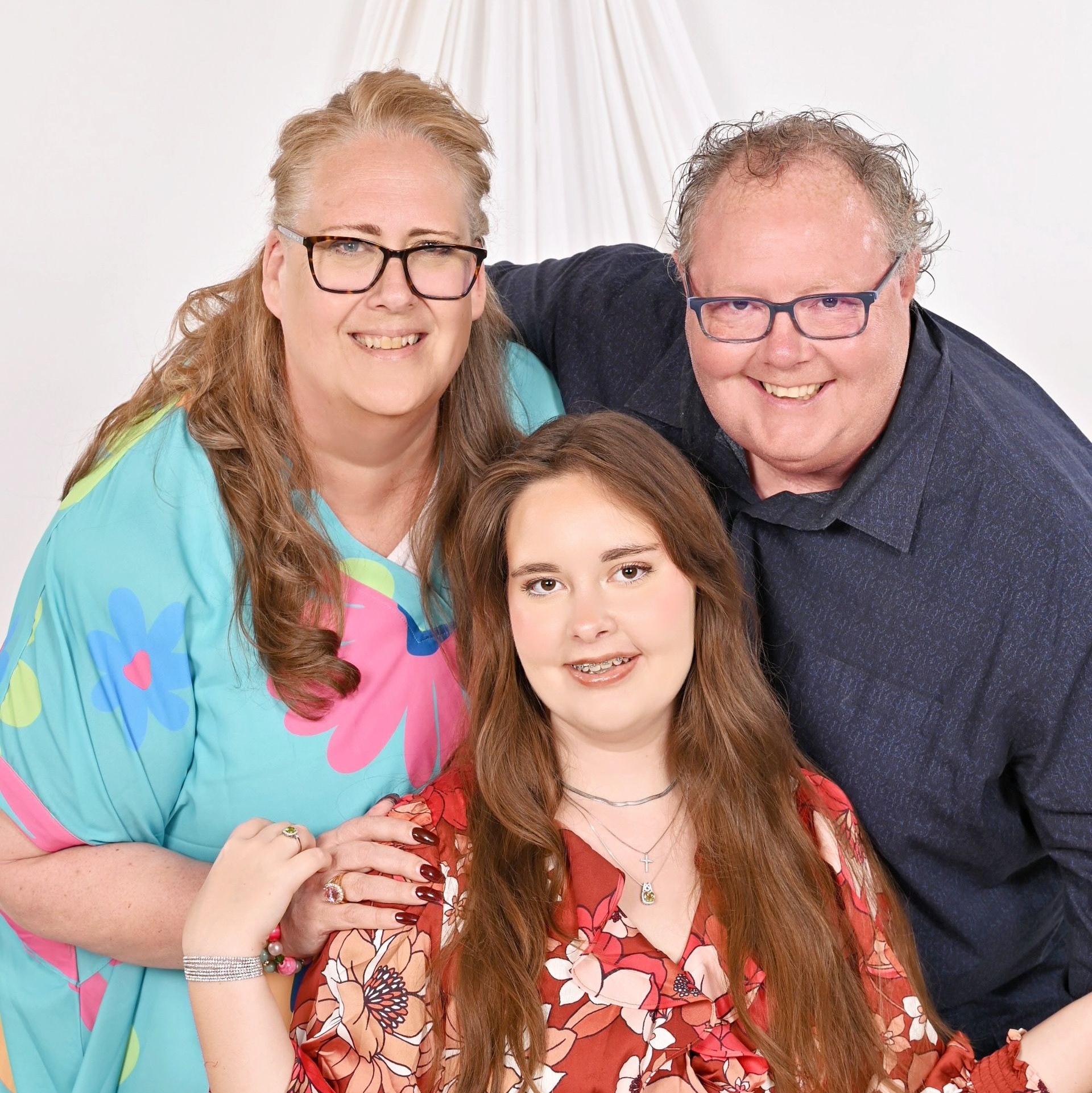 A smiling family of three posing for a portrait against a white background.