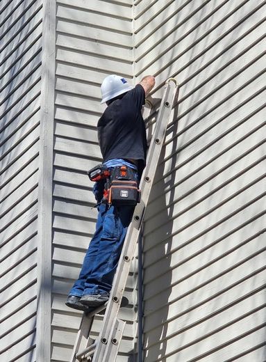 A man is standing on a ladder on the side of a building.