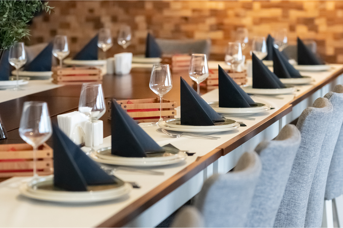 A long table with plates , napkins , glasses and utensils on it.