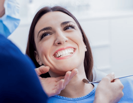 A woman is smiling while having her teeth examined by a dentist.