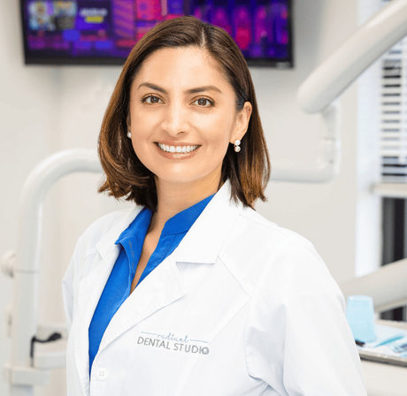 A woman in a lab coat is smiling in a dental office.