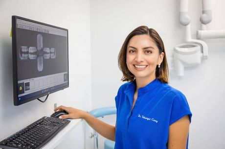 A woman in a blue shirt is standing in front of a computer monitor.