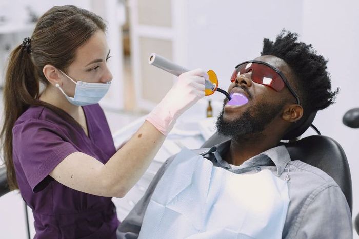 A man is sitting in a dental chair getting his teeth examined by a female dentist.