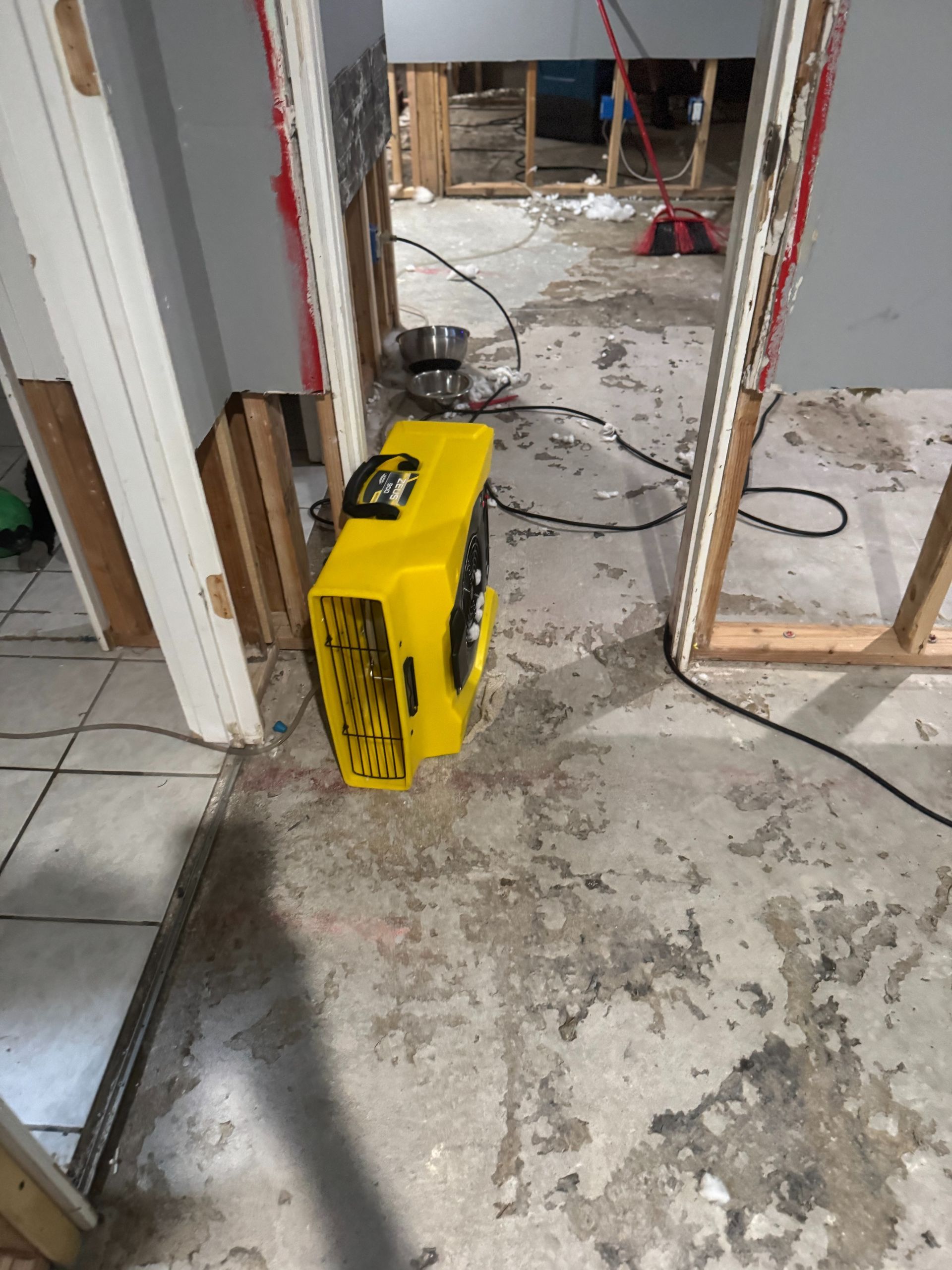 Yellow dehumidifier on a dusty floor in a partially demolished room with exposed studs and debris