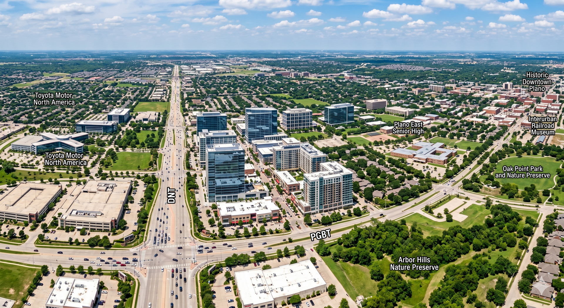 Aerial view of a suburban city with wide roads, modern buildings, and green parks under a blue sky