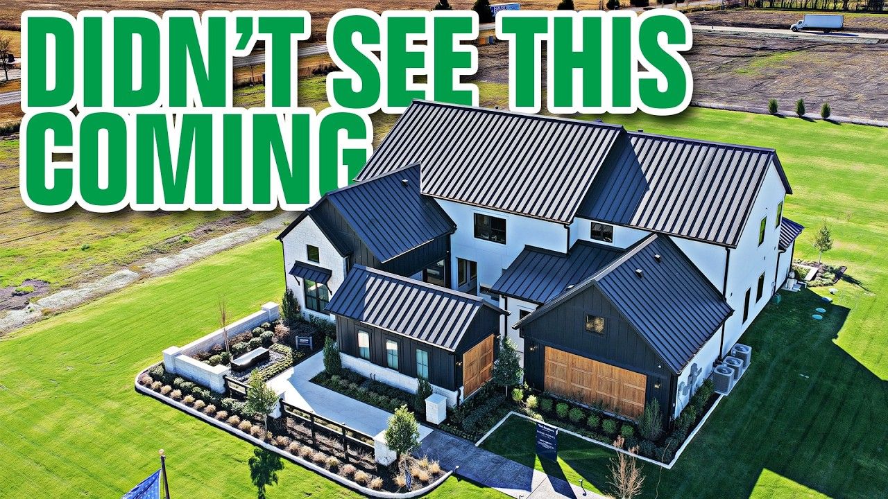 Aerial view of a modern farmhouse with black metal roof and white siding, set on green lawn.